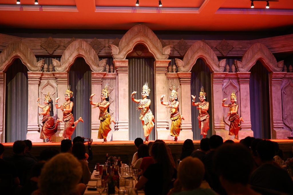 A line of Apsara dancers in gold costumes on stage at the dinner show in Siem Reap