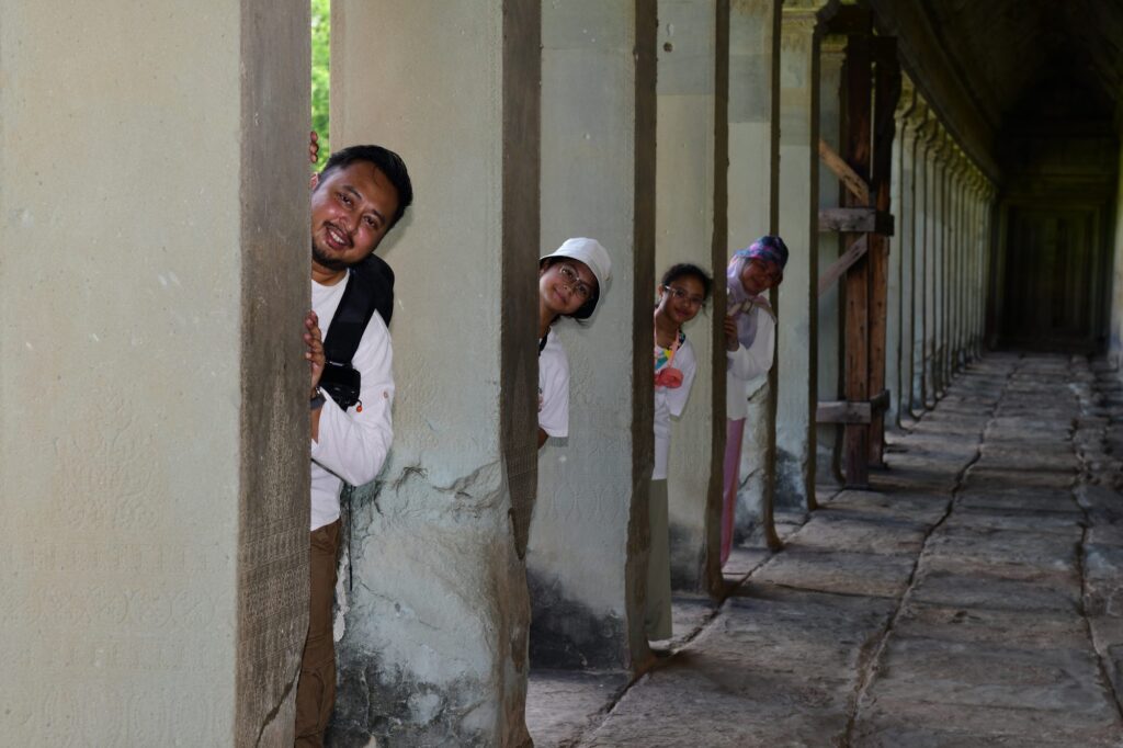 The family peeking out from behind a row of stone pillars in an Angkor Wat corridor