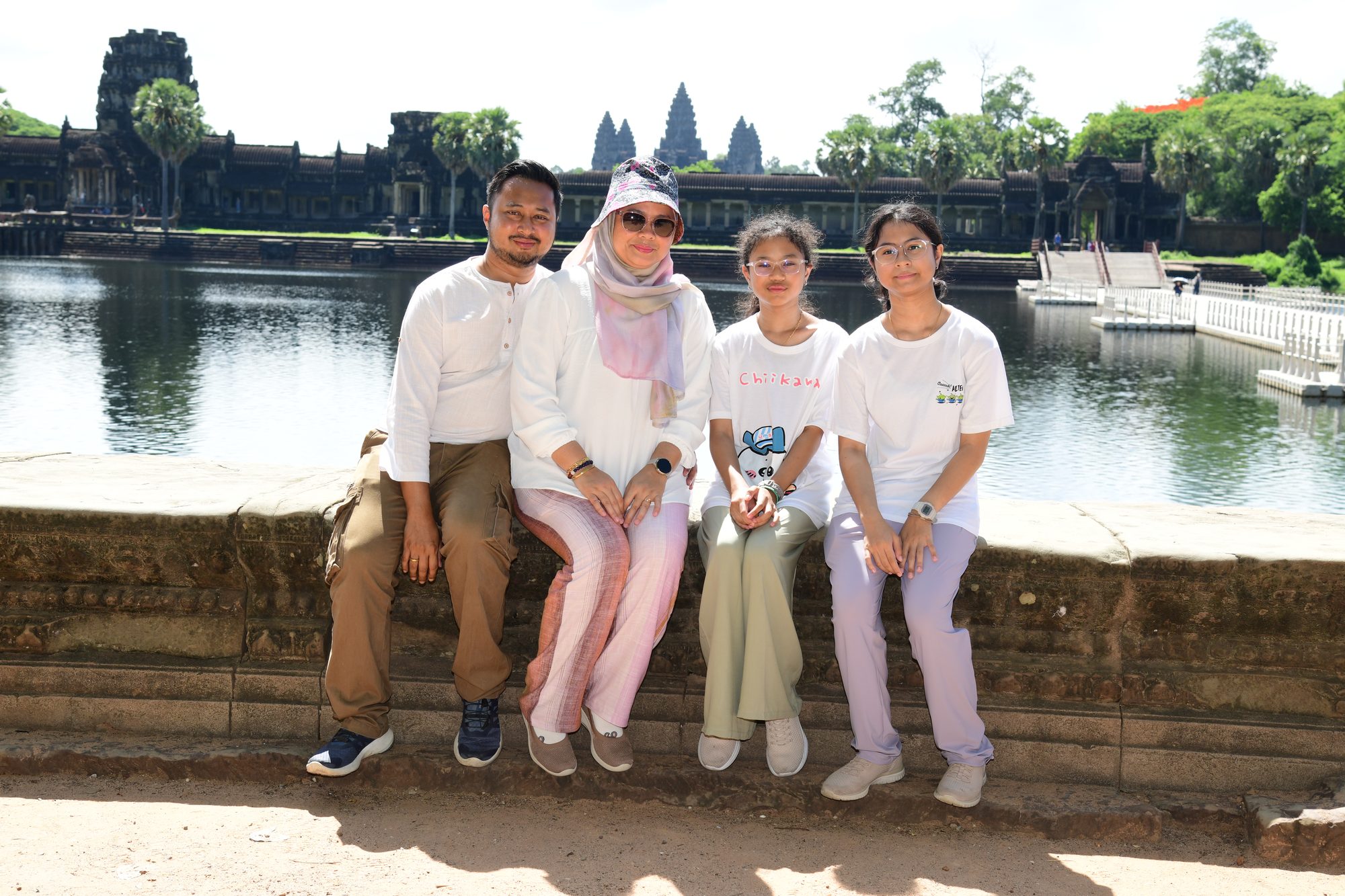 The family sitting on the moat wall with the towers of Angkor Wat behind them