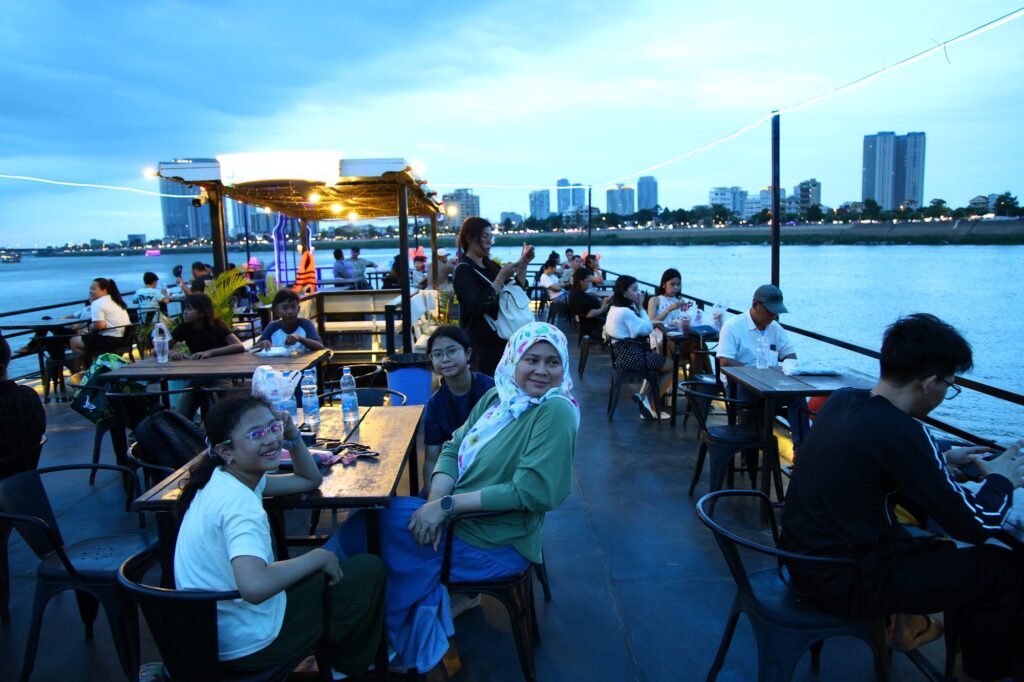Family at a table on the deck of a dinner cruise on the Mekong, with the Phnom Penh skyline behind